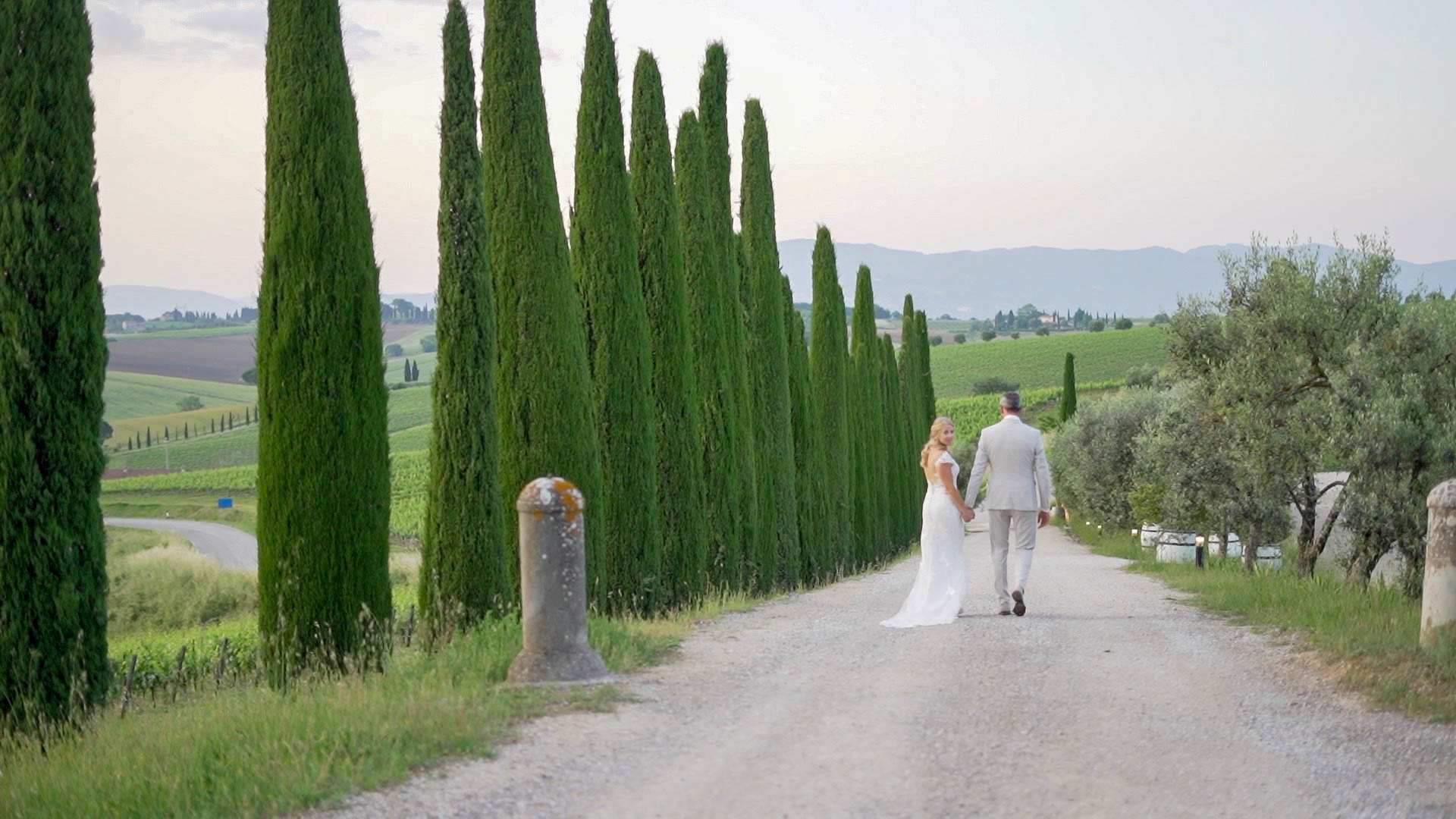 Eva e Martijn A couple during their Tuscan vineyard wedding celebration near Montepulciano in Tuscany. The bride and groom walk down the cypress-lined aisle, surrounded by wineries, vineyards, and rolling green hills.
